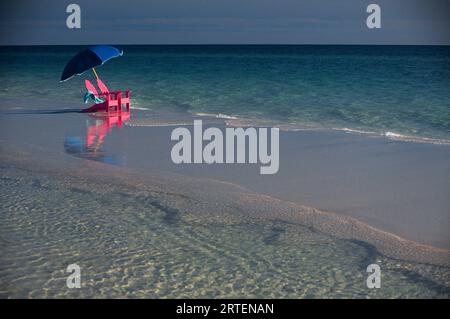 Paire de chaises rouges et un parasol sur une plage au bord de l'eau ; Floride, États-Unis d'Amérique Banque D'Images