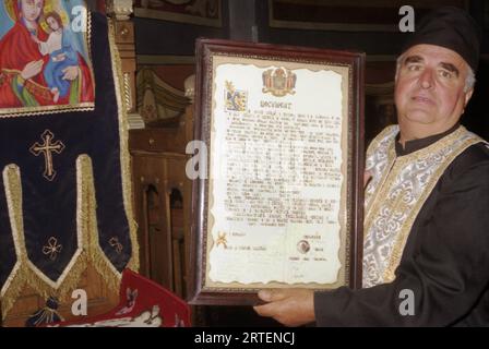 Traisteni, commune de Valea Doftanei, comté de Prahova, Roumanie, 2003. Père Ioan Albu, prêtre à l'église orthodoxe locale 'Saint voïvodes', tenant un document de 1988 de la reconsécration de l'église. Banque D'Images