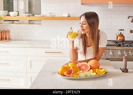 Femme buvant du jus d'agrumes frais dans la cuisine Banque D'Images