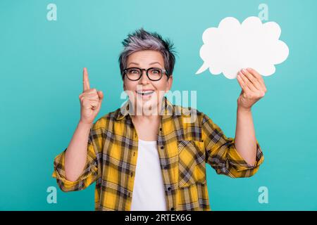 Portrait photo de belle dame senior tenir papier nuage doigt pointer vers le haut porter vêtement jaune plaid tendance isolé sur fond de couleur cyan Banque D'Images