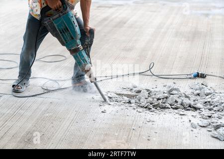 Travailleur sur le chantier de construction démolissant le béton avec le marteau de cric électrique. Banque D'Images