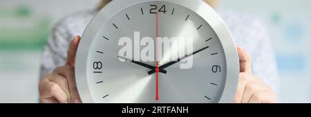 Elle tient une horloge ronde près de son corps. Banque D'Images