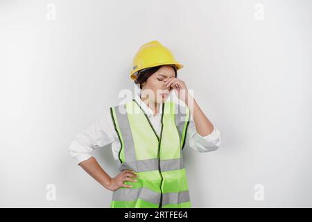 Un portrait de femme asiatique de travail porte un casque de sécurité et un gilet, semble stressé et déprimé, fond blanc isolé. Banque D'Images