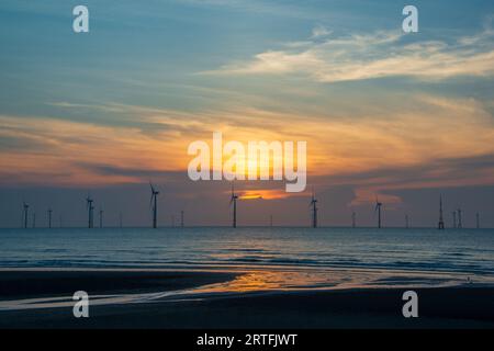 Les ventilateurs des éoliennes tournent au-dessus de la mer étincelante. Nuages dynamiques au coucher du soleil. Un parc éolien offshore au large de la côte nord-ouest de Taïwan. Un de pow vert Banque D'Images