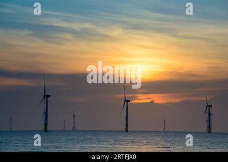 Les ventilateurs des éoliennes tournent au-dessus de la mer étincelante. Nuages dynamiques au coucher du soleil. Un parc éolien offshore au large de la côte nord-ouest de Taïwan. Un de pow vert Banque D'Images