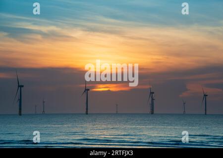 Les ventilateurs des éoliennes tournent au-dessus de la mer étincelante. Nuages dynamiques au coucher du soleil. Un parc éolien offshore au large de la côte nord-ouest de Taïwan. Un de pow vert Banque D'Images