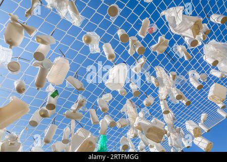 Conteneurs en plastique dans le filet de pêche contre le ciel bleu - concept d'ordures, pollution de l'eau, question environnementale Banque D'Images