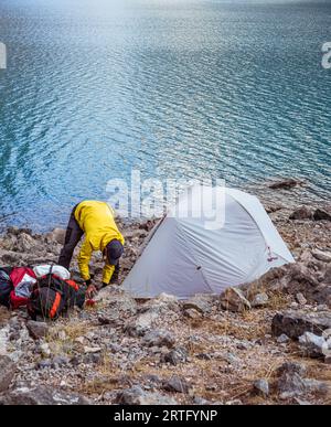 Un randonneur installe une tente dans un camp sur un lac de montagne Banque D'Images