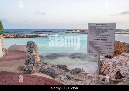 Un signe d'instructions sur un rivage rocheux d'une plage sur une île tropicale. Banque D'Images