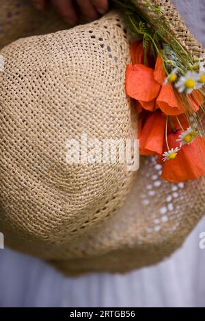 Gros plan extrême d'un chapeau de paille avec des coquelicots rouges et des fleurs de camomille Banque D'Images