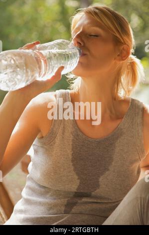 Gros plan d'une jeune femme à boire de l'eau d'une bouteille avec ses yeux fermés Banque D'Images