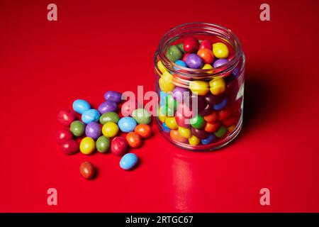 Nature morte bonbons multicolores dans un bocal en verre sur fond rouge Banque D'Images