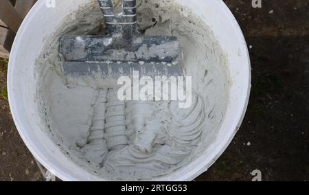 une spatule en forme dans un seau en plastique avec une solution élastique visqueuse comme jeu de plâtrier pour la finition, remuant le mastic dans le récipient Banque D'Images