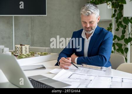Homme architecte avec barbe travaillant sur un certain projet, assis à table dans le bureau devant son ordinateur portable. Banque D'Images
