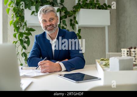 Homme architecte avec barbe travaillant sur un certain projet, assis à table dans le bureau devant son ordinateur portable. Banque D'Images