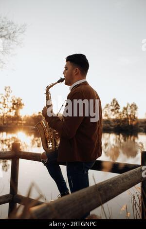 jeune musicien jouant le saxophone au coucher du soleil dans le lac Banque D'Images