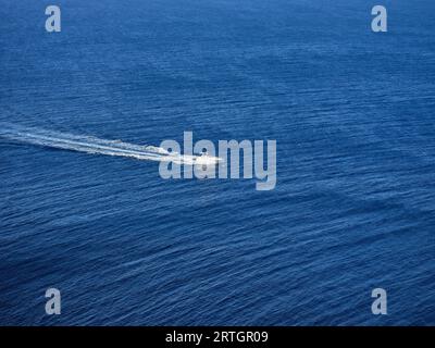Vue à grand angle du bateau blanc flottant dans l'eau de mer ondulée bleue et laissant derrière lui un sentier mousseux Banque D'Images