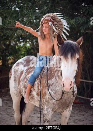 Jeune garçon à cheval dans les rênes tout en regardant loin de la campagne avec des arbres verts et pointant du doigt à côté Banque D'Images