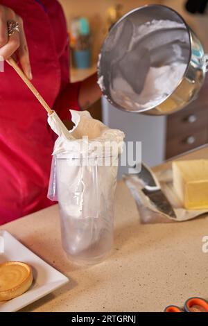 Confiseur sans visage prenant la crème fouettée hors du bol et remplissant le sac de pâtisserie pour la décoration de tartelettes dans la boulangerie maison Banque D'Images