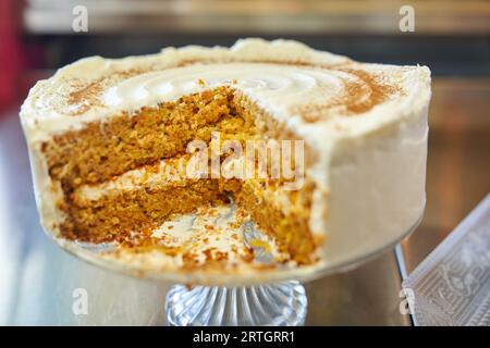 Gros plan de gâteau aux carottes avec morceau coupé de celui-ci recouvert de délicieuse crème au beurre et servi sur support en verre Banque D'Images