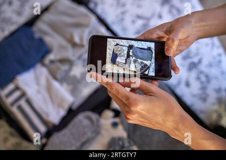 Vue de dessus de la récolte anonyme touriste prenant la photo de valise ouverte placée sur le lit sur le téléphone portable dans la mise au point sélective Banque D'Images