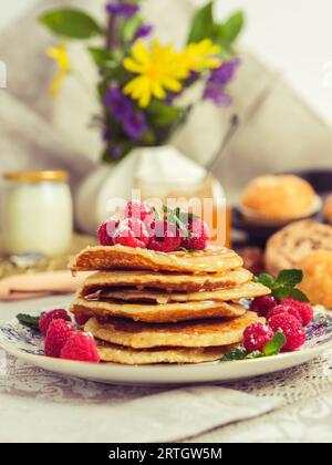 Assiette avec pile de crêpes délicieuses décorées de framboises et de feuilles de menthe servi pour le petit déjeuner sur table dans la cuisine rustique Banque D'Images