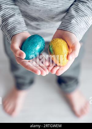 D'en haut d'un enfant méconnaissable montrant des œufs enveloppés dans du papier d'aluminium préparé pour les vacances de Pâques Banque D'Images