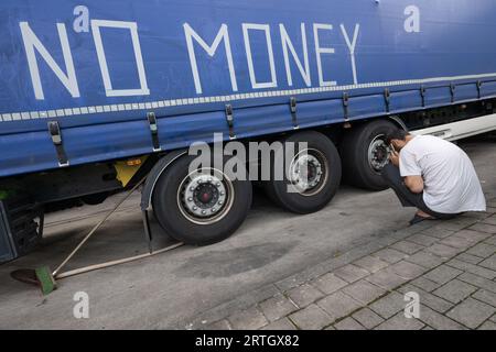 13 septembre 2023, Hesse, Gräfenhausen : un chauffeur de camion s'accroupe dans le parking de la zone de service de Gräfenhausen devant un camion sur lequel ses collègues ont écrit "pas d'argent". Les chauffeurs, qui viennent de plusieurs pays d’Europe de l’est, sont assis dans leurs camions sur le parking de la zone de service de Gräfenhausen depuis près de deux mois, attendant le paiement de leur salaire. Photo : Boris Roessler/dpa Banque D'Images