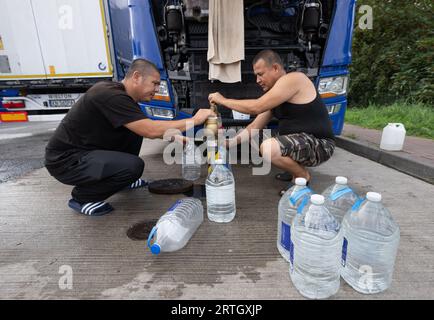 13 septembre 2023, Hesse, Gräfenhausen : les camionneurs remplissent des bouteilles d'eau potable sur le parking de la zone de service de Gräfenhausen. Les chauffeurs, qui viennent de plusieurs pays d’Europe de l’est, attendent dans leurs camions sur le parking de la zone de service de Gräfenhausen depuis près de deux mois, en attendant le paiement de leur salaire. Photo : Boris Roessler/dpa Banque D'Images