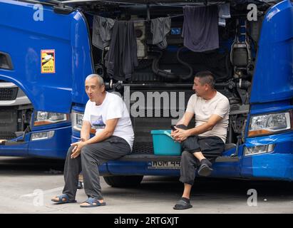 13 septembre 2023, Hesse, Gräfenhausen : les chauffeurs de camion sont assis dans le parking de la zone de service de Gräfenhausen devant la grille ouverte d'un camion, devant lequel ils ont également suspendu leurs vêtements pour sécher. Les chauffeurs, qui viennent de plusieurs pays d’Europe de l’est, attendent dans leurs camions sur le parking de la zone de service de Gräfenhausen depuis près de deux mois, en attendant le paiement de leur salaire. Photo : Boris Roessler/dpa Banque D'Images