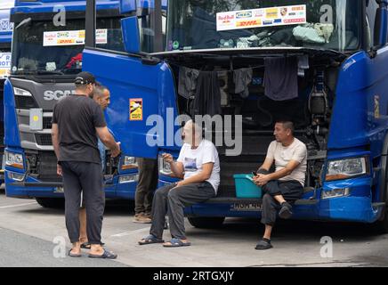 13 septembre 2023, Hesse, Gräfenhausen : les chauffeurs de camion sont assis dans le parking de la zone de service de Gräfenhausen devant la grille ouverte d'un camion, devant lequel ils ont également suspendu leurs vêtements pour sécher. Les chauffeurs, qui viennent de plusieurs pays d’Europe de l’est, attendent dans leurs camions sur le parking de la zone de service de Gräfenhausen depuis près de deux mois, en attendant le paiement de leur salaire. Photo : Boris Roessler/dpa Banque D'Images