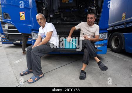 13 septembre 2023, Hesse, Gräfenhausen : les chauffeurs de camion sont assis dans le parking de la zone de service de Gräfenhausen devant la grille ouverte d'un camion, devant lequel ils ont également suspendu leurs vêtements pour sécher. Les chauffeurs, qui viennent de plusieurs pays d’Europe de l’est, attendent dans leurs camions sur le parking de la zone de service de Gräfenhausen depuis près de deux mois, en attendant le paiement de leur salaire. Photo : Boris Roessler/dpa Banque D'Images