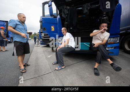 13 septembre 2023, Hesse, Gräfenhausen : les chauffeurs de camion sont assis dans le parking de la zone de service de Gräfenhausen devant la grille ouverte d'un camion, devant lequel ils ont également suspendu leurs vêtements pour sécher. Les chauffeurs, qui viennent de plusieurs pays d’Europe de l’est, attendent dans leurs camions sur le parking de la zone de service de Gräfenhausen depuis près de deux mois, en attendant le paiement de leur salaire. Photo : Boris Roessler/dpa Banque D'Images