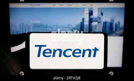 Personne tenant smartphone avec le logo de la société chinoise Tencent Holdings Ltd. Sur l'écran en face du site Web. Concentrez-vous sur l'affichage du téléphone. Banque D'Images