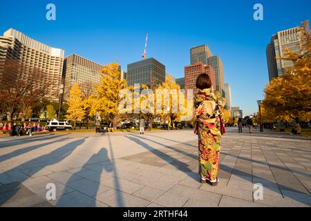 Une femme asiatique portant un kimono traditionnel japonais debout avec des feuilles de ginko ou du feuillage d'automne près de la gare de Tokyo, au Japon Banque D'Images