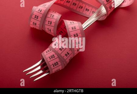 Ruban à mesurer enroulé autour d'une fourchette couchée sur un fond rouge. Bonne nutrition appropriée. Régime pour le concept de perte de poids. Banque D'Images