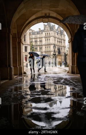 LONDRES - 24 avril 2023 : les gens avec des parapluies se reflètent dans une flaque d'eau sous l'arche à Horse Guards Parade un jour de pluie. Banque D'Images