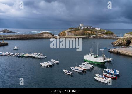 Vue sur le port de Tapia de Casariego et le phare en arrière-plan avec un ciel nuageux. Banque D'Images