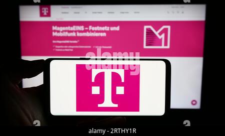 Personne détenant un téléphone portable avec le logo de la société de télécommunications Deutsche Telekom AG sur l'écran devant la page Web. Concentrez-vous sur l'affichage du téléphone. Banque D'Images