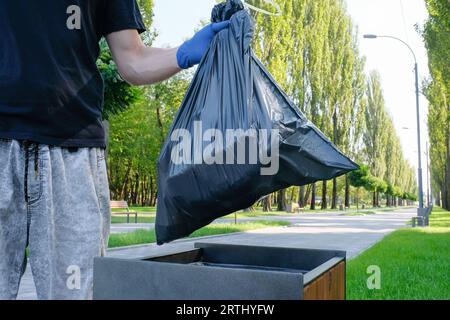 La main du volontaire tenant un sac poubelle noir met dans le panier. Problèmes environnementaux. Banque D'Images