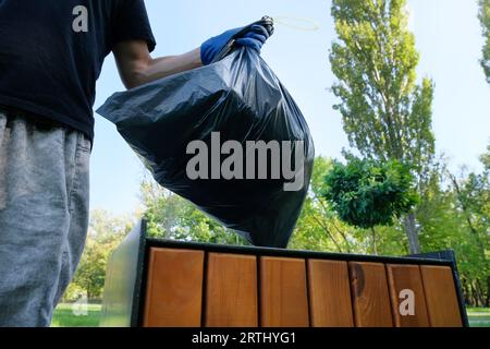 Une main tenant un sac poubelle noir met dans un panier. Concept de protection de l'environnement Banque D'Images