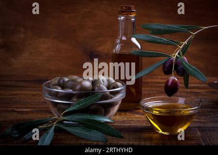 Bol de l'huile d'olive et olives violettes sur fond de bois foncé Banque D'Images