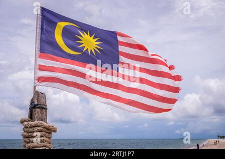 Drapeau malaisien attaché sur le poteau agitant sur la plage de l'île de Langkawi par temps nuageux Banque D'Images