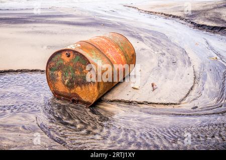 Le baril de pétrole rouillé sur une plage en partie noire illustre la pollution de l'environnement par les déversements de pétrole Banque D'Images