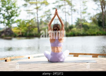 femme sportive pratiquant le yoga sur une jetée au bord d'un lac, assise méditant, partie de la série. Banque D'Images
