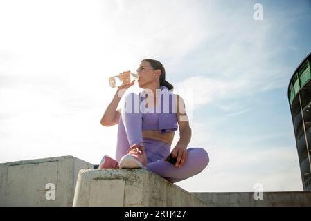 un coureur sportif boit de l'eau dans une bouteille en verre, dans un cadre urbain Banque D'Images