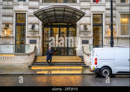 LONDRES - 24 avril 2023 : un portier se tient sur les marches de l'entrée de l'hôtel Corinthia, prolongeant un accueil chaleureux par un jour de pluie au cœur de l'ic Banque D'Images