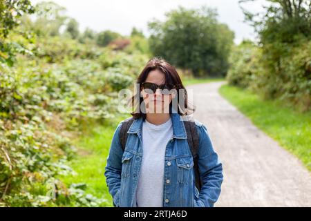 Portrait d'une belle femme d'âge moyen dans une veste en denim et des lunettes de soleil sur une route de campagne Banque D'Images