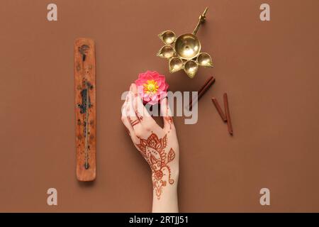 Main féminine avec lampe diya, bâton d'encens, cannelle et fleur de lotus pour la célébration de Divaly sur fond brun Banque D'Images