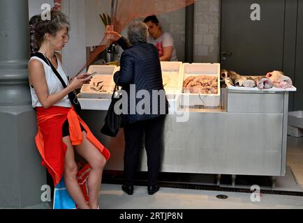 Femme debout vérifiant son téléphone debout attendant à l'intérieur du marché historique à deux niveaux, Mercado do Bolhão, avec un étal de poisson frais servant un autre client Banque D'Images